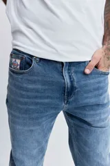 Pantalón de jean corte regular, color azul medio con efecto lavado, de tiro medio y cierre frontal con botón y cremallera.
