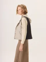Chaleco con capucha, presenta una espalda de pelo sintético en color marrón oscuro con etiqueta de cuero negra y una capucha de tela tipo denim azul. Diseño original con mezcla de texturas.
