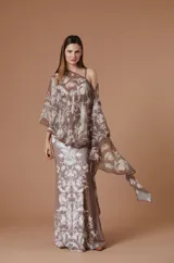 Vestido largo de fiesta con capa integrada, confeccionado en tela fluida con estampado botánico barroco en tonos marrones y crema. El diseño presenta un corte ajustado al cuerpo con escote asimétrico y una capa superpuesta que aporta movimiento y elegancia.