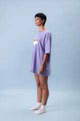 Remera oversize color lila con estampa frontal gráfica en tonos marrón y crema. Presenta cuello redondo, mangas cortas y un corte holgado.