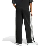 Pantalón de mujer Adidas tipo jogging en color negro, con diseño de malla transpirable, corte ancho y franjas blancas laterales con las clásicas tres tiras de la marca. Cuenta con cintura elástica con cordón de ajuste y logo bordado en la pierna.