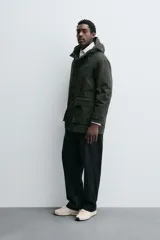 Parka color verde militar de corte relaxed fit, confeccionada en tejido de algodón con interior acolchado. Cuenta con cuello subido, capucha ajustable con cordón, cierre frontal de cremallera oculta por solapa con botones a presión y amplios bolsillos frontales de plastrón con solapa.