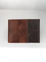 Billetera masculina confeccionada en cuero, con diseño bicolor en tonos marrón claro y oscuro. Presenta un detalle grabado de un búho en la parte frontal.