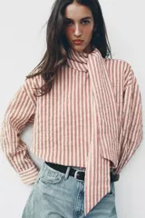 Camisa de rayas rojas y blancas, cuello redondo con lazada integrada y manga larga.