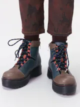 Botas de cuero estilo trekking, en combinación de colores verde, marrón y gris, con plataforma de goma negra, cordones bicolor inspirados en cuerdas de escalada y pasadores en tono rojizo.