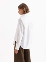 Camisa de poplin color blanco, con cuello clásico, cierre frontal de botones y mangas largas con puños. Presenta un diseño bordado de pequeñas llamas distribuidas por toda la prenda.