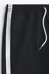 Short deportivo negro con bandas laterales blancas, cintura elástica con cordón ajustable blanco y bolsillos laterales.