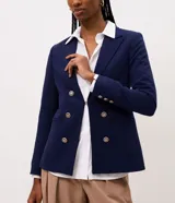 Blazer cruzado de sastrería en color azul marino, con corte slim y estructura entallada. Presenta solapas de muesca, cierre frontal con seis botones dorados metálicos con relieve, bolsillos con solapa en los laterales y mangas largas.
