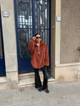 Buzo de corderito color marrón, con cuello alto y cierre frontal parcial. Presenta un diseño holgado con mangas largas y un parche decorativo en el frente.