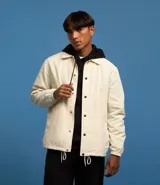 Campera color crema de poliéster con cuello inglés, abotonadura delantera con botón a presión, mangas largas con puño elástico, bajo elástico y cordón para ajustar.