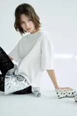 Camiseta oversize de cuello redondo y manga corta, con bajo asimétrico que presenta una aplicación de lentejuelas brillantes en contraste.