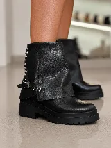 Bota corta de cuero negro con diseño de polaina superpuesta, detalle de tachas metálicas en el lateral y correa con hebilla ajustable. Cuenta con suela track de goma y taco cuadrado.