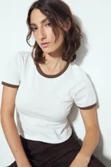 Remera cropped blanca de manga corta, con cuello redondo y terminaciones en contraste de color marrón en cuello y mangas. Inspirada en los clásicos de los años 80.