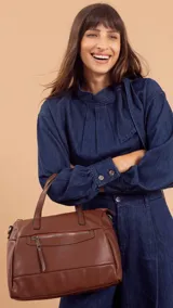 Cartera de mano y hombro color beige, de material símil cuero, con forma estructurada y redondeada. Posee dos asas cortas superiores y una correa larga ajustable y desmontable. Cuenta con un bolsillo exterior con cierre en la parte frontal.