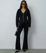 Campera femenina de punto roma en color negro, con diseño acinturado y efecto peplum. Presenta cierre frontal con cremallera metálica, escote en V y bolsillos delanteros.