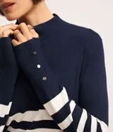 Blusa alargada de punto con diseño rayado horizontal en azul marino y blanco, cuello alto y manga larga con detalles de botones en los puños.