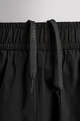 Pantalón jogger negro de corte regular, confeccionado en tejido técnico con algodón. Presenta cintura elástica ajustable con cordón interior, bolsillos laterales y puños elásticos en los tobillos. Posee un pequeño logo estampado en contraste en la pierna derecha.