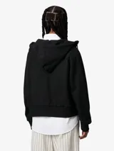 Campera con capucha de tejido bouclé color crema, corte boxy y holgado, con cierre frontal de cremallera. Posee bolsillo canguro con remaches metálicos y etiqueta cuadrada de piel sintética en el frente.