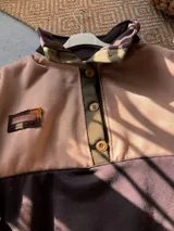 Buzo oversize de friza de algodón y poliéster, con diseño colorblock en tonos verde militar, marrón y rosado. Cuenta con cuello alto, solapa con botones frontales y mangas largas.