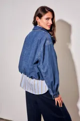 Campera bomber de jean con corte oversize, cierre frontal y cuello alto con botones a presión. Presenta mangas amplias y puños ajustados.