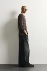Jeans de denim de algodón color gris con efecto lavado, de corte relaxed barrel fit y tiro medio. Presenta diseño amplio con pinzas en las rodillas y costuras curvas, cierre frontal con botones y cinco bolsillos tradicionales.