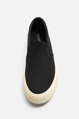 Zapatilla slip-on negra de tejido de algodón con elásticos laterales y suela color crema.