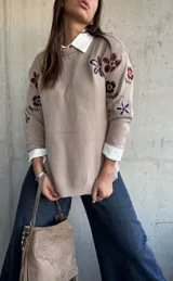 Sweater de punto color beige con cuello redondo y diseño de flores bordadas en tonos oscuros en el frente y las mangas.