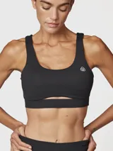 Top deportivo negro con escote redondo, tirantes anchos y un corte debajo del busto que crea una abertura. Incluye logo blanco en el pecho.