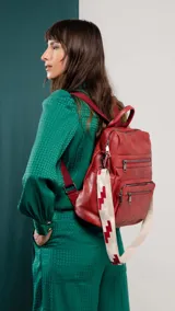 Mochila de símil cuero color marrón con apertura superior y tres bolsillos frontales con cierres metálicos. Cuenta con bolsillos laterales y una correa de galón con diseño geométrico, regulable y extraíble, que permite su uso como bandolera.