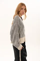 Buzo de tejido de punto con diseño geométrico en relieve, cuello redondo y mangas largas abullonadas con puños ajustables mediante lazos. Presenta un borde inferior en tejido acanalado de color crudo.