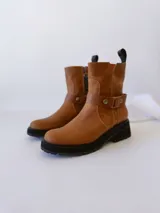 Bota de cuero color marrón con suela de goma negra, cierre lateral y pulsera desmontable con hebilla.