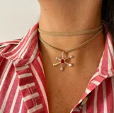 Collar de tiento negro con dije metálico plateado en forma de estrella o molécula, con una piedra central de color y terminaciones esféricas.