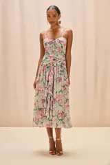 Vestido midi de tirantes finos con escote recto y detalle fruncido en el centro del busto. Presenta un diseño drapeado en la cintura y falda fluida con volado frontal, confeccionado en tela liviana con estampado floral en tonos verdes y rosados.