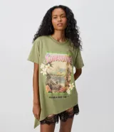 Remera oversize de algodón en color verde militar, con cuello redondo, mangas cortas y bajo asimétrico. Presenta un estampado frontal de paisaje tropical con flores y las inscripciones "Sunshine" y "Having a Good Time".