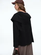 Buzo negro de algodón con diseño de efecto superpuesto, que simula una prenda atada sobre los hombros. Presenta cuello redondo, mangas largas con puños ajustados y un corte holgado.