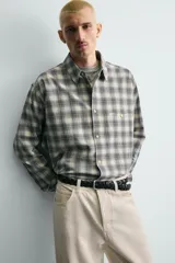 Camisa de corte boxy fit confeccionada en tejido de algodón con elasticidad. Presenta un diseño a cuadros, cuello solapa, manga larga con puños abotonados, bolsillo de vivo en el pecho y cierre frontal con botones.