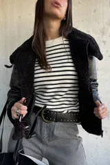 Campera tipo gamulán de cuero sintético negro con interior y detalles de cuello y puños en piel sintética negra. Presenta cierre frontal, correas ajustables en los puños y diseño de corte clásico.