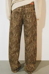 Jeans de tiro medio con diseño de perneras curvas y corte recto, confeccionados en denim con estampado paisley en tonos marrones y beige. Presentan diseño clásico de cinco bolsillos, trabillas para cinturón y cierre frontal con cremallera y botón metálico.