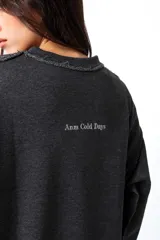 Buzo gris oscuro, estilo sweatshirt, con cuello redondo y terminaciones al corte en cuello, puños y cintura. Presenta un bordado en el frente.