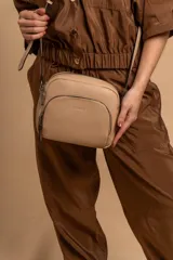Bandolera de diseño compacto en color beige, confeccionada en material símil cuero con textura granulada. Cuenta con un bolsillo frontal con cierre y correa larga regulable.