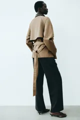 Gabardina corta de sarga color marrón claro, con doble botonadura, cuello de solapa en contraste de color negro con efecto cuero, bolsillos laterales con solapa y cinturón ajustable para anudar en la cintura.