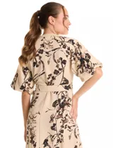 Vestido maxi de crepe color beige con estampado floral en tonos marrones y negros. Presenta cuello a la base, escote en V, abertura central con botones y cintura con lazo de ajuste y hebilla.