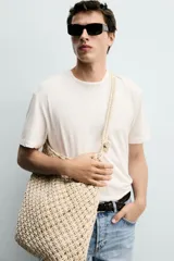 Bolso de hombro confeccionado en tejido trenzado de algodón con diseño de macramé, asa de hombro con detalle de nudo y bolsillo interior plano.