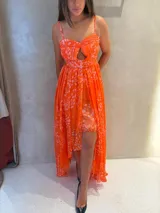 Vestido midi de tirantes finos con diseño asimétrico, presentando una falda corta interior y una sobrecapa larga de gasa con abertura frontal. El diseño incluye un escote corazón con detalle de abertura central y un estampado abstracto en tonos naranja y rosa.