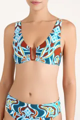 Top de bikini con escote en V profundo y detalle de herraje metálico en forma de U en el centro. Presenta un estampado geométrico multicolor en tonos terracota, azul y blanco.