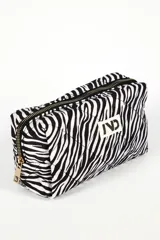 Neceser rectangular acolchado con estampado de cebra en blanco y negro, cierre superior con cremallera negra y tirador dorado, y parche blanco con logo en el frente.