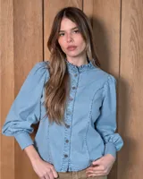 Camisa de jean de corte entallado, con cuello alto con volados, cierre frontal con botones y mangas abullonadas con puños ajustados.