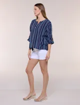 Blusa Erika de algodón con estampado de rayas en tonos azules, rosados y amarillos. Presenta cuello redondo con escote en V y botones frontales, mangas cortas decoradas con una fila de botones en los laterales y dobladillo asimétrico.