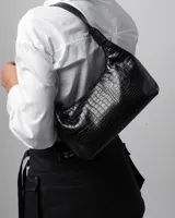 Cartera tipo baguette de cuero sintético color negro, con diseño curvo, cierre superior y asa corta regulable con hebilla metálica.