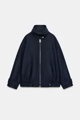 Chaqueta bomber de corte holgado confeccionada en tejido con lana, color azul marino. Presenta cuello subido, cierre frontal con cremallera metálica, bolsillos delanteros y detalle de trabillas con botones metálicos en el ruedo.